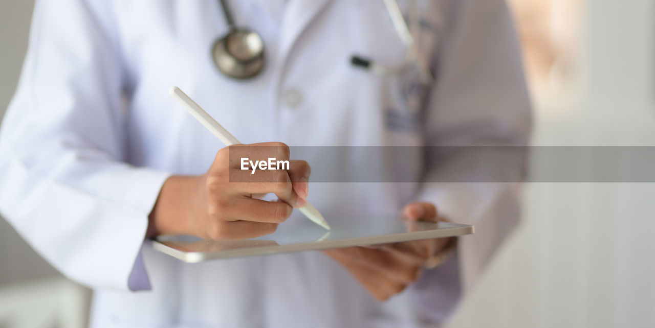 Midsection of doctor using digital tablet in clinic