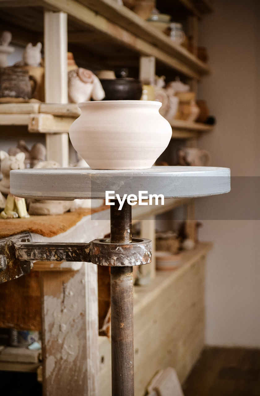 Clay pot close-up in the foreground and shelves with pottery - on the second