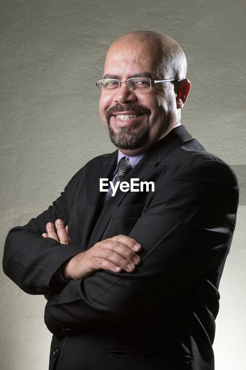 Portrait of mature bald businessman smiling while standing against gray wall