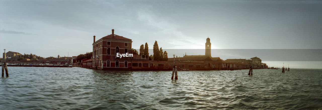 View of buildings by sea against cloudy sky