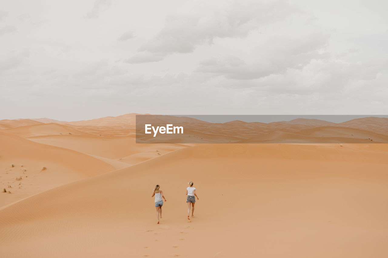 PEOPLE WALKING ON SAND DUNE AGAINST SKY