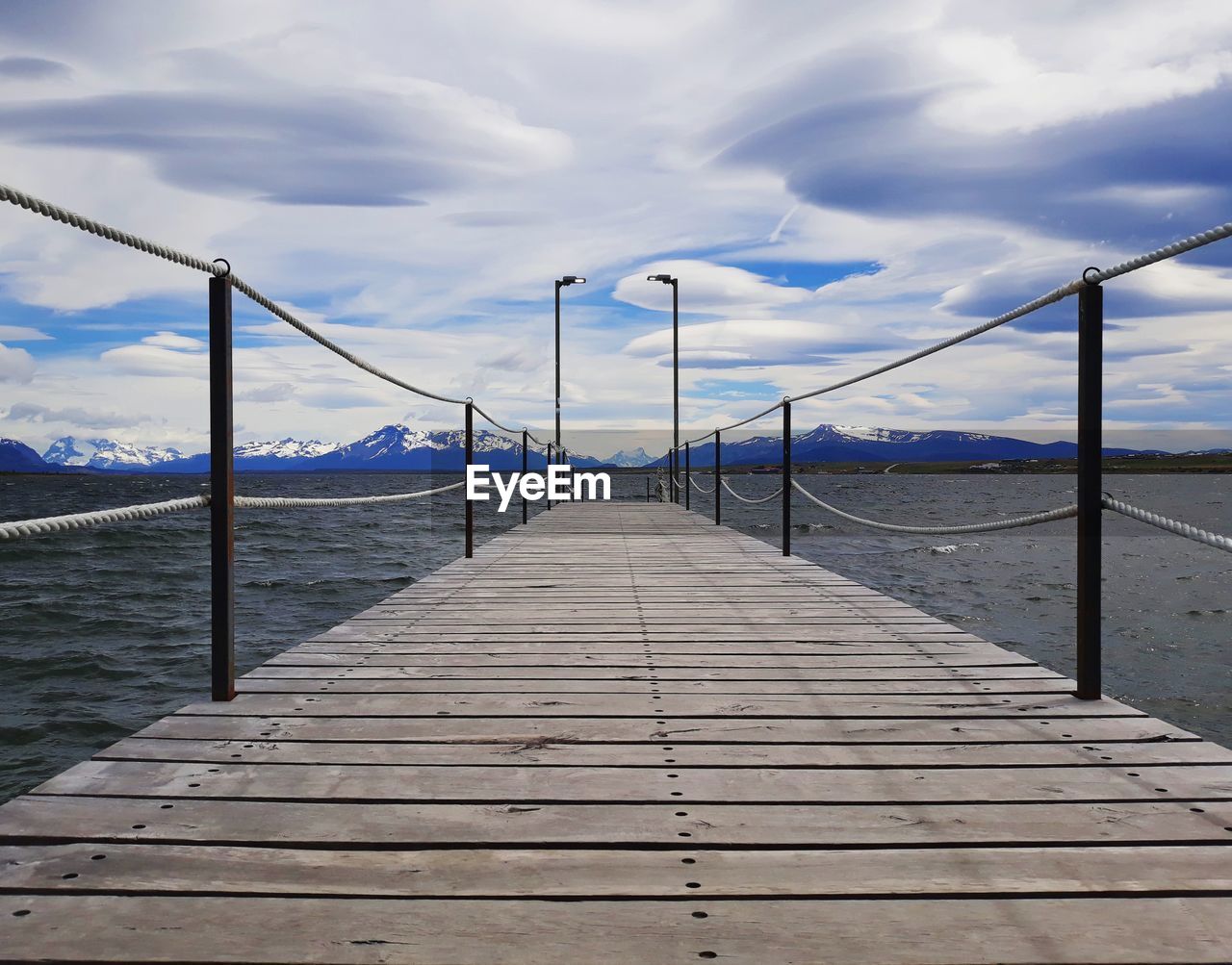 Wood pier with a cloudy sky and snow capped mountains in the background