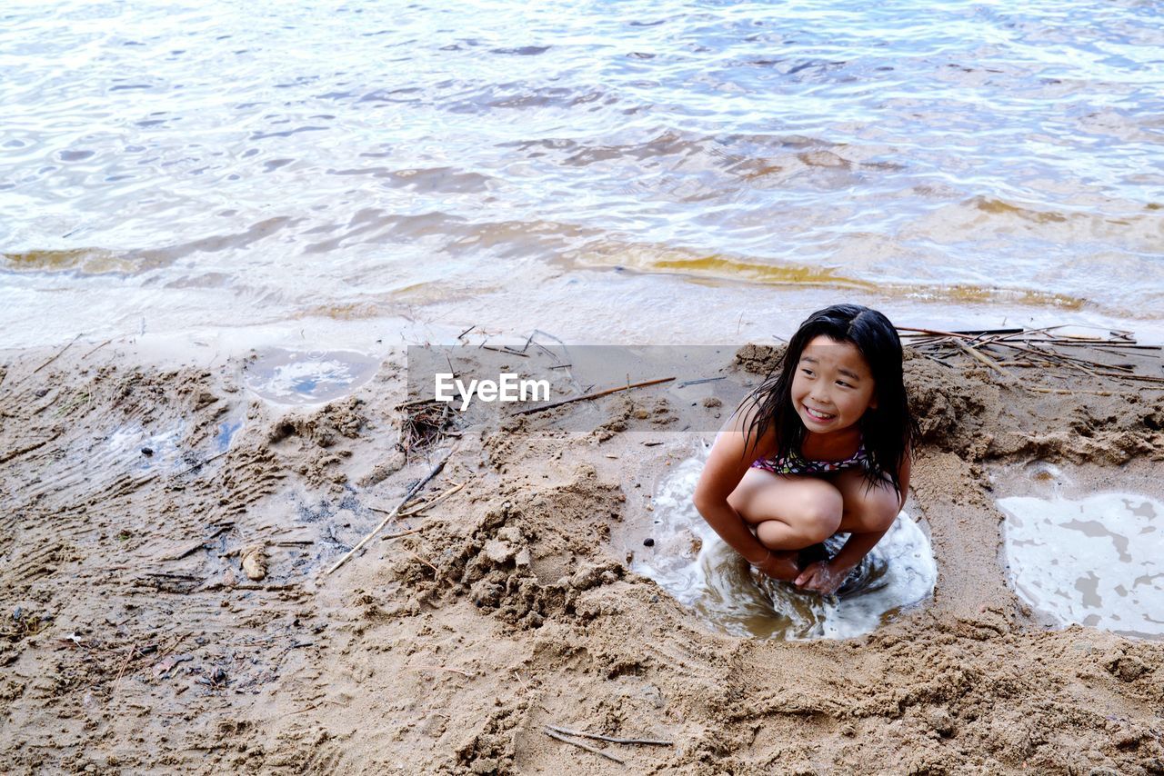 High angle view of happy girl crouching on beach