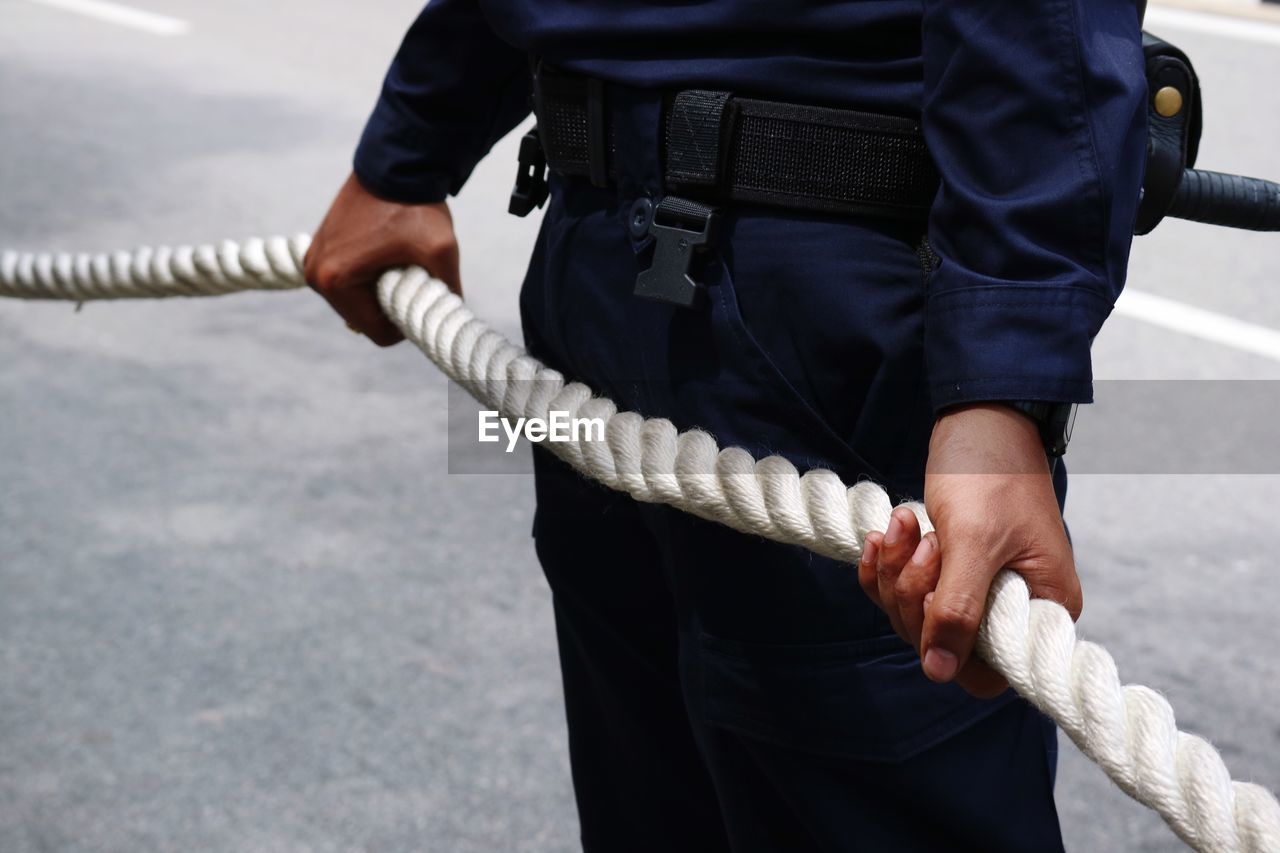 Midsection of man in uniform holding rope