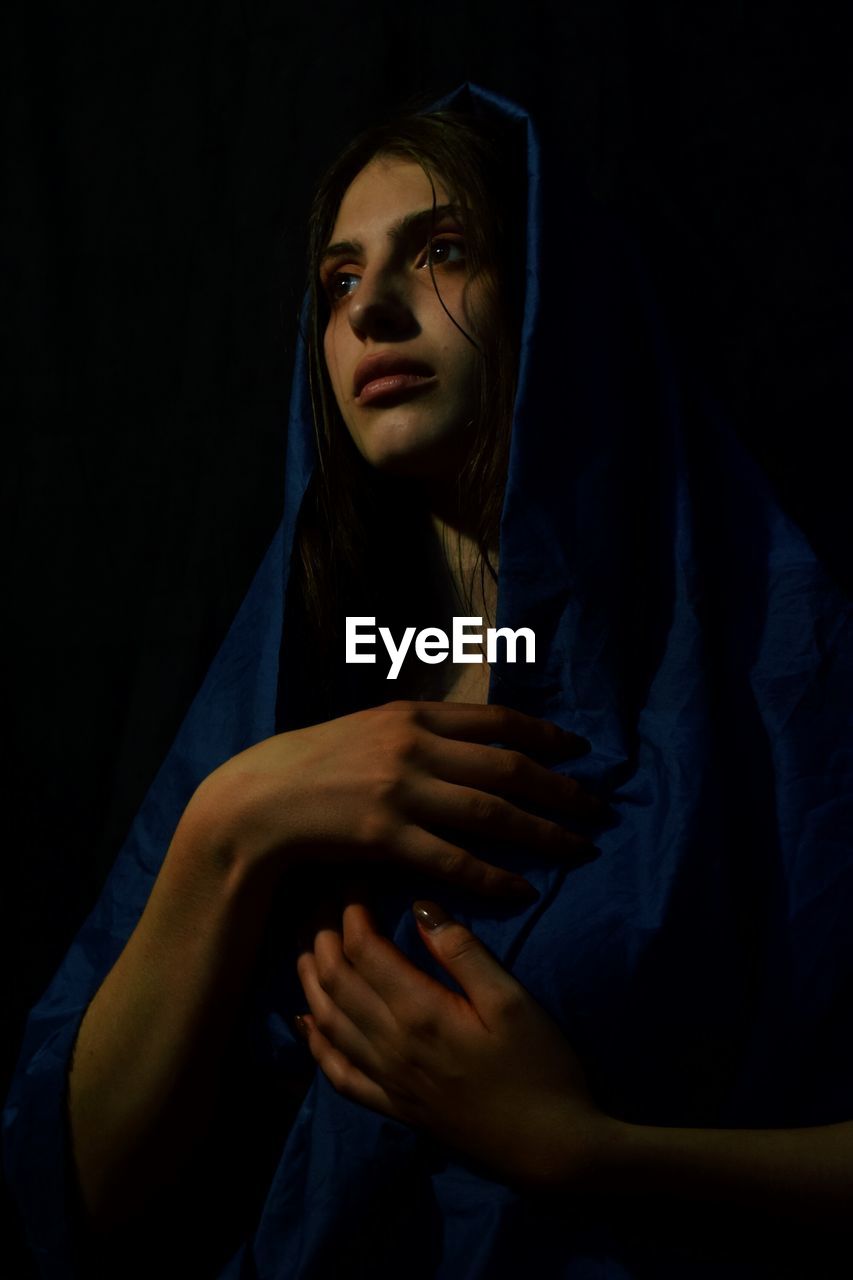 Thoughtful woman with hand on breast standing against black background