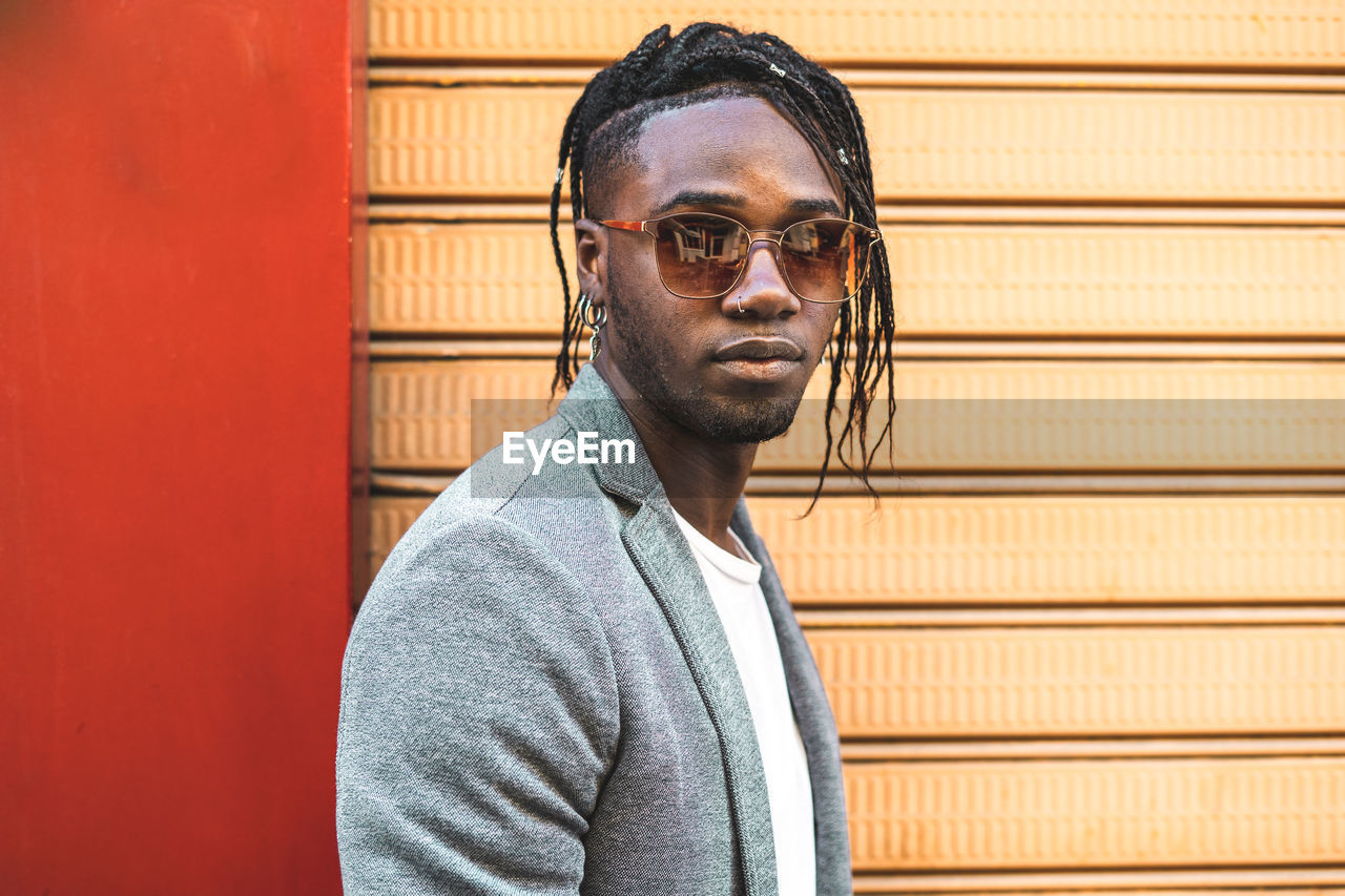 Portrait of young man wearing sunglasses against wall