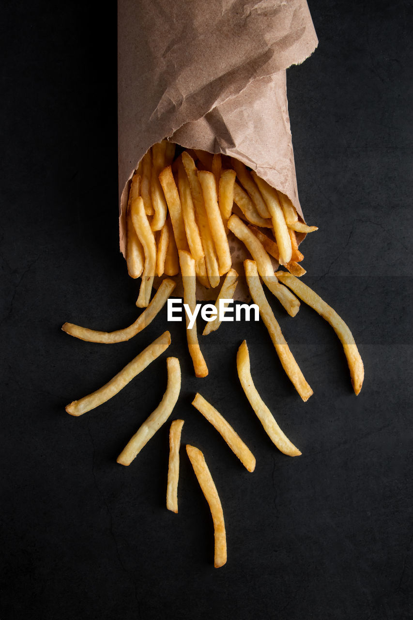 Hot crispy fries in a paper bag on a black background. tasty american fast food.