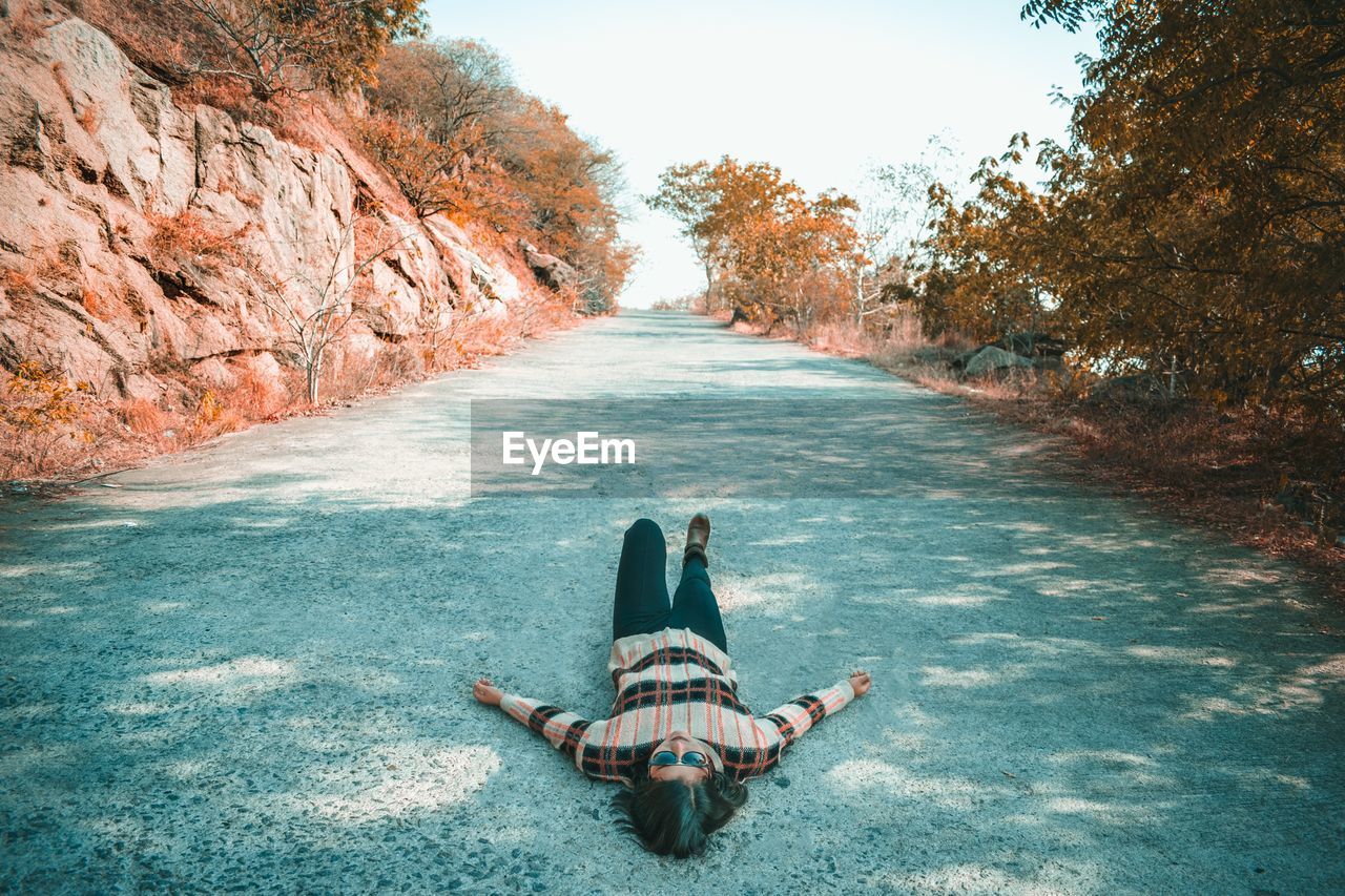 Woman lying on road against sky