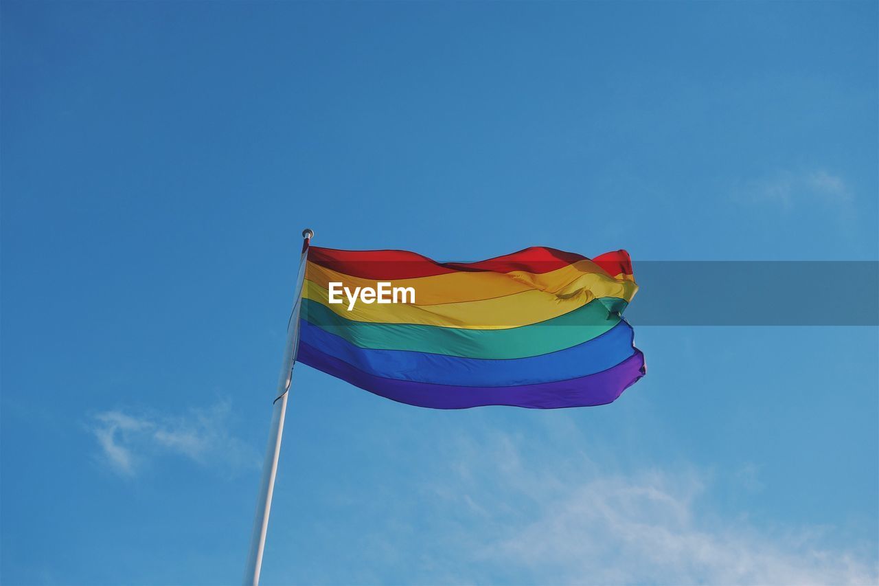 Low angle view of rainbow flag against blue sky