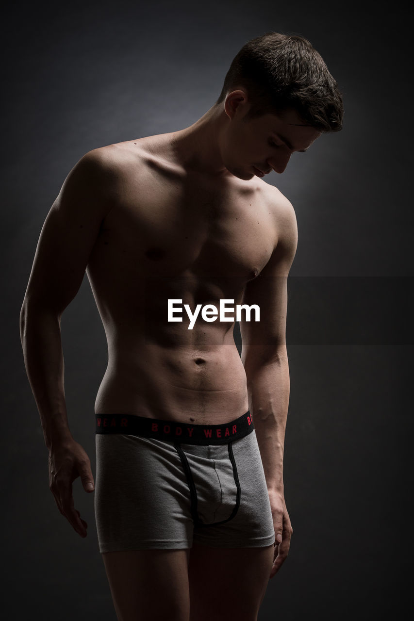 FULL LENGTH OF SHIRTLESS MAN AGAINST BLACK BACKGROUND