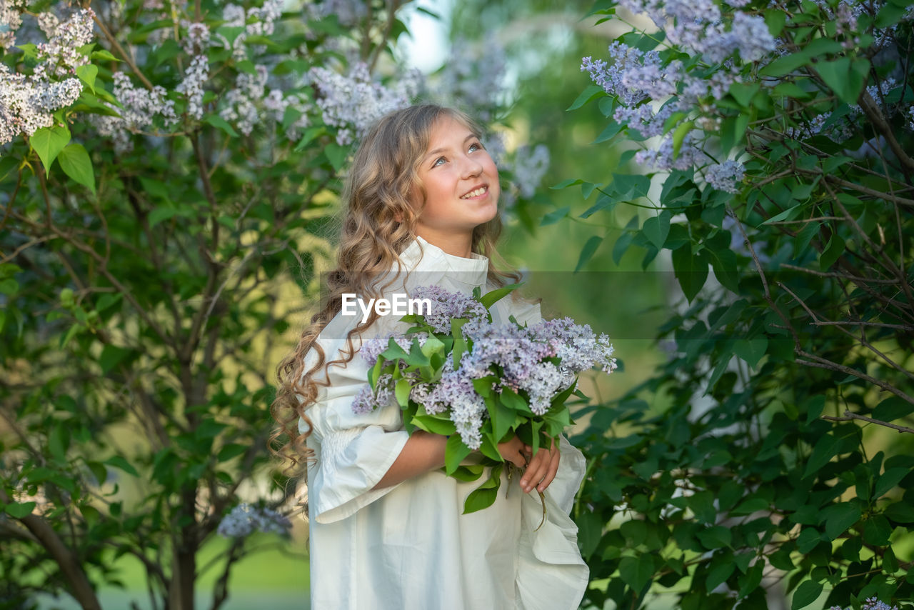 PORTRAIT OF WOMAN STANDING BY FLOWERING PLANT
