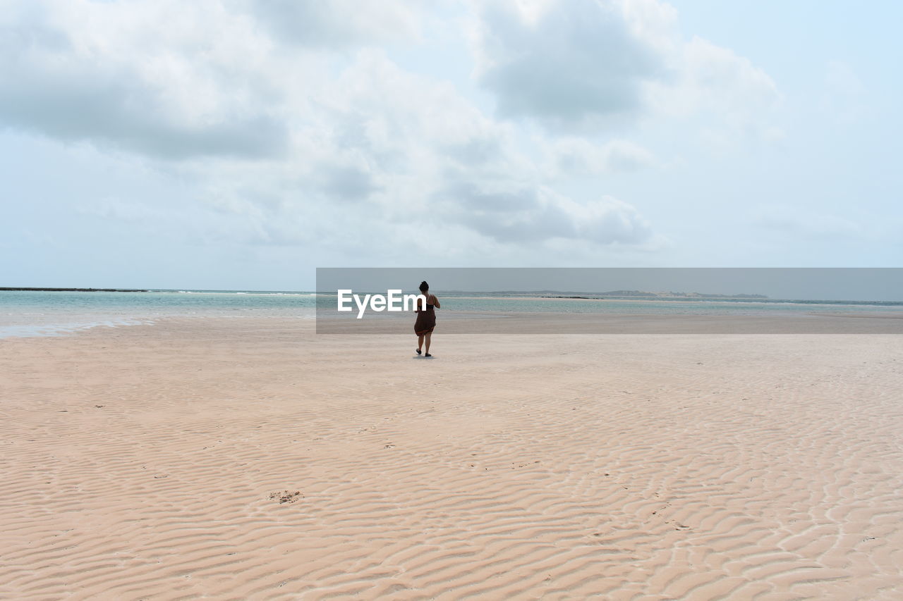 Rear view of woman standing on beach against sky