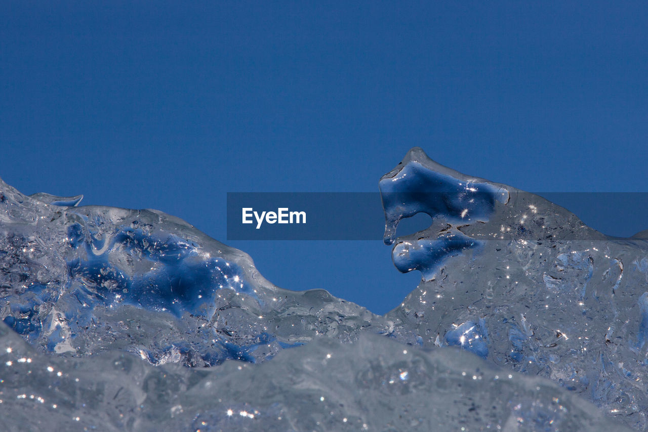 CLOSE-UP OF FROZEN WATER SPLASHING AGAINST BLUE SKY