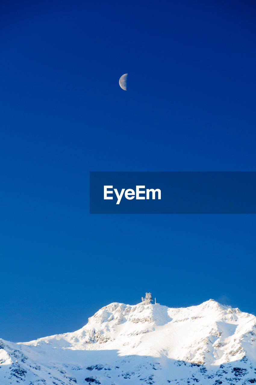 Low angle view of snowcapped mountains against clear blue sky