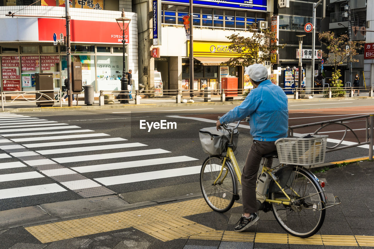 REAR VIEW OF MAN CROSSING BICYCLE