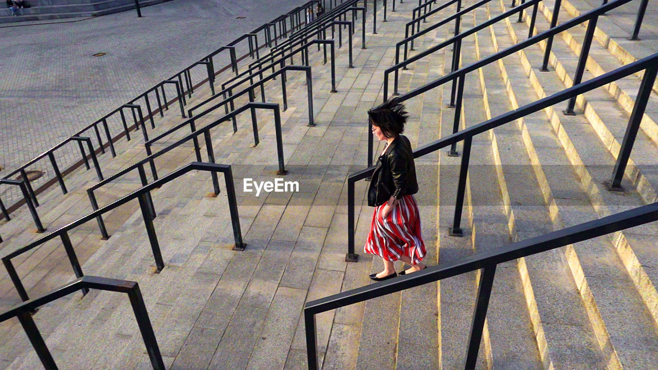 Full length of woman wearing striped skirt and jacket on steps amidst railing in city