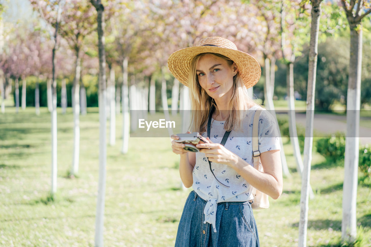 Young beautiful stylish woman photographer in a hat with a digital camera in a city park. 