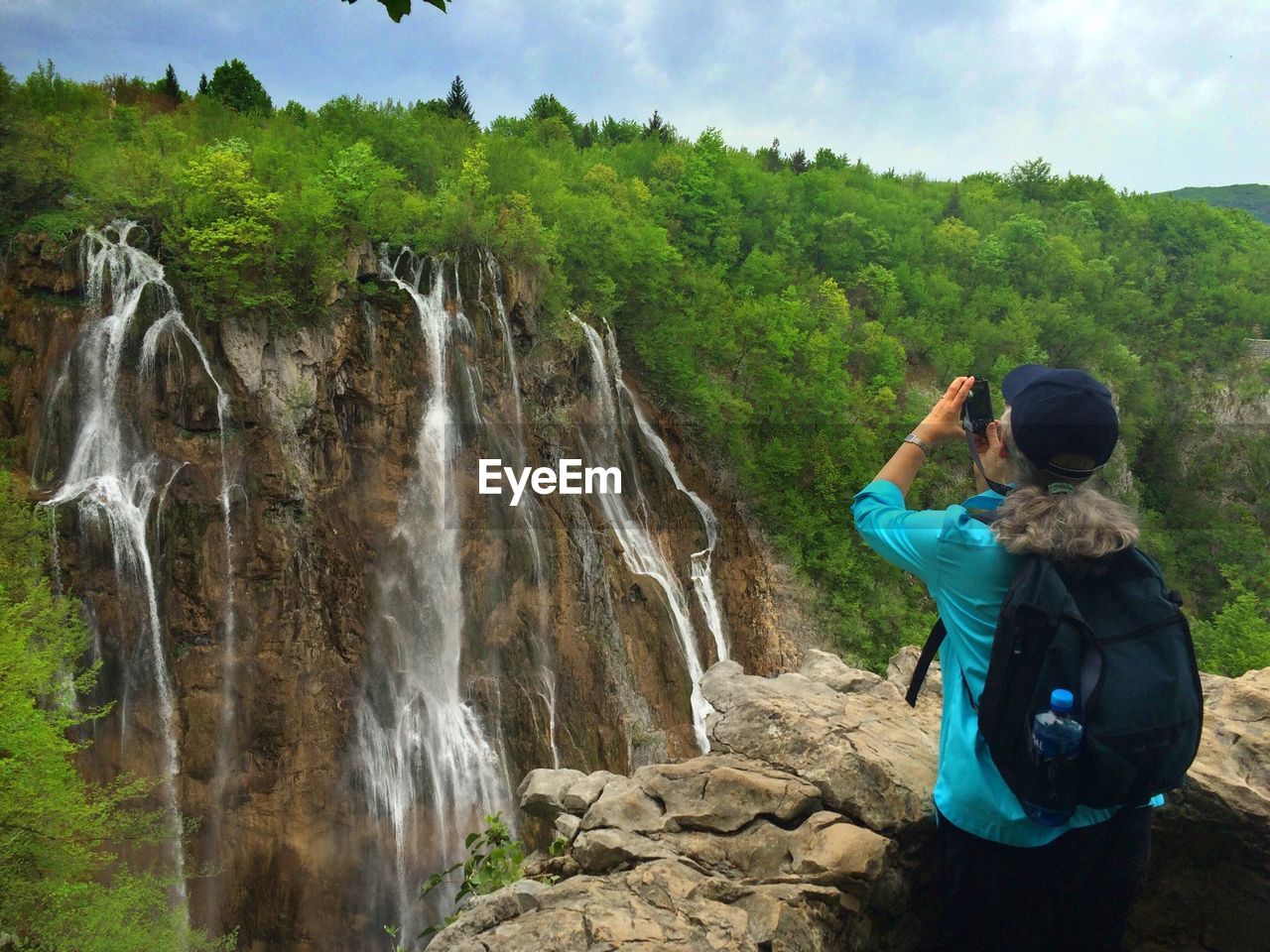 Rear view of woman photographing waterfall at plitvice lakes national park