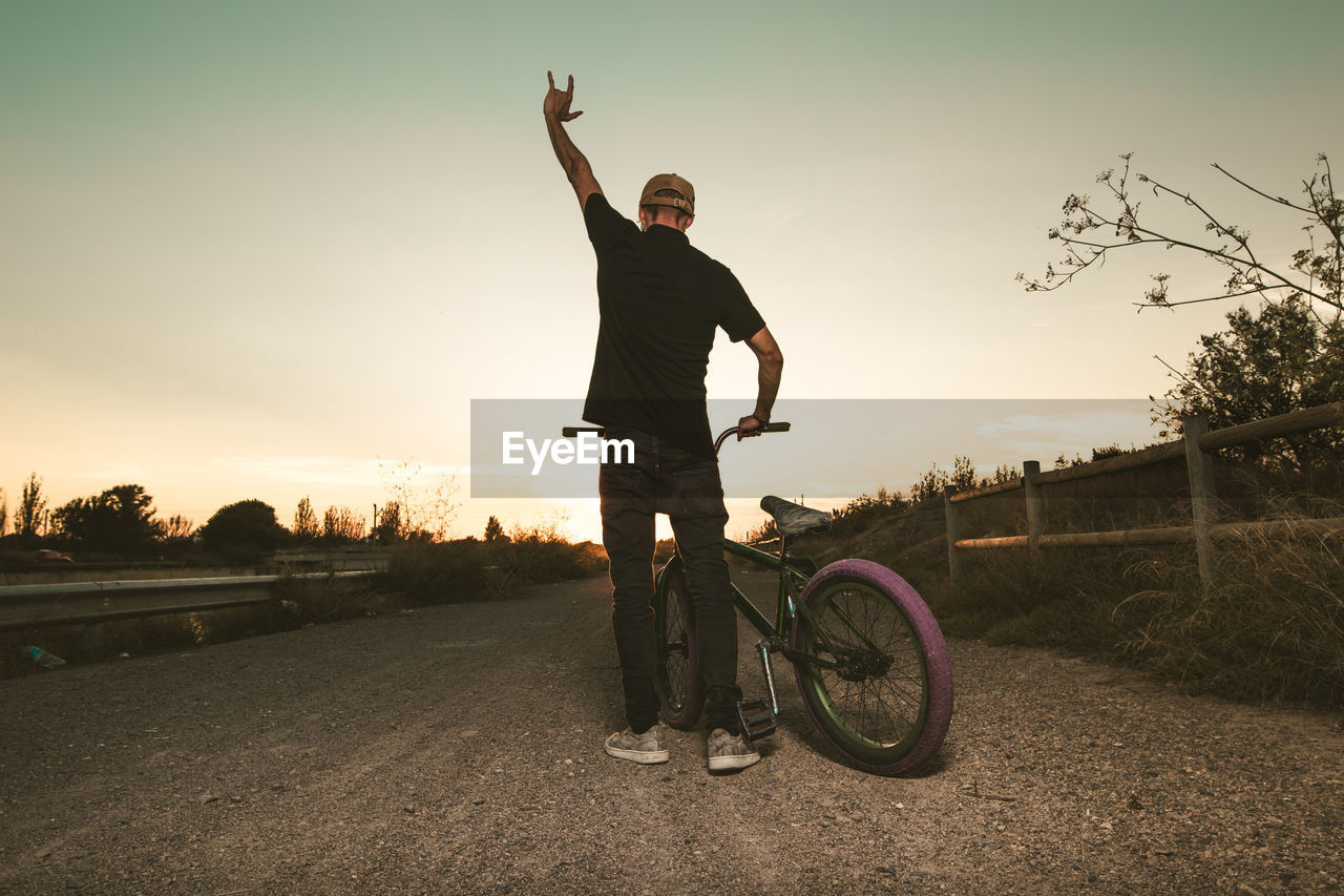 MAN RIDING BICYCLE ON STREET AGAINST SKY