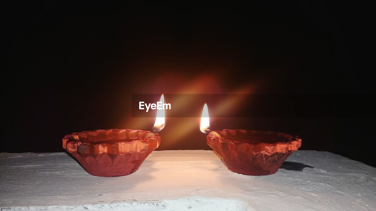 CLOSE-UP OF ILLUMINATED BURNING CANDLES ON BLACK