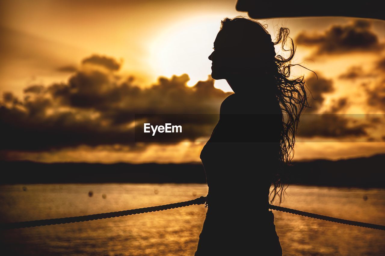 Silhouette woman standing by sea against sky during sunset