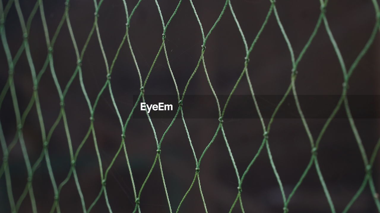 CLOSE-UP OF CHAINLINK FENCE AGAINST BLURRED BACKGROUND