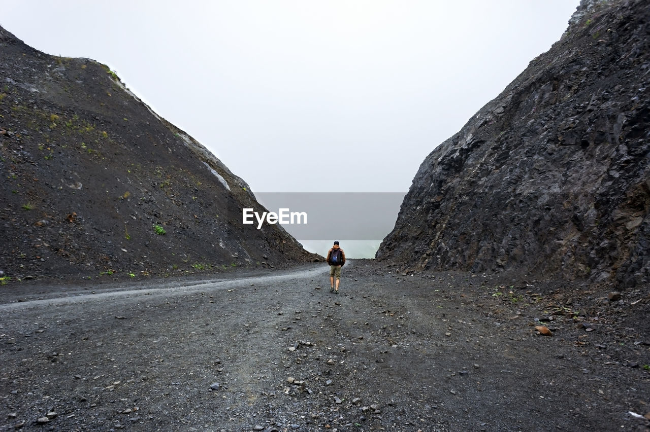 Young man from the back with backpack walking along a path between two rocks. mountain travel alone