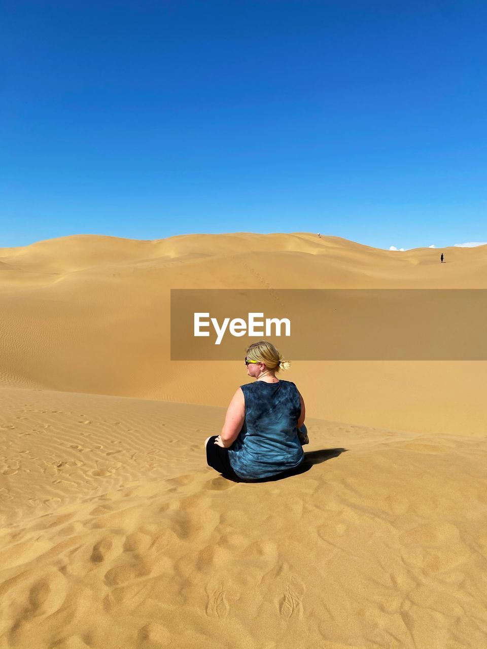 Woman sitting on sand dune in desert against clear sky