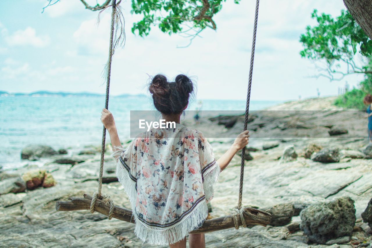 Rear view of woman on swing by sea against sky