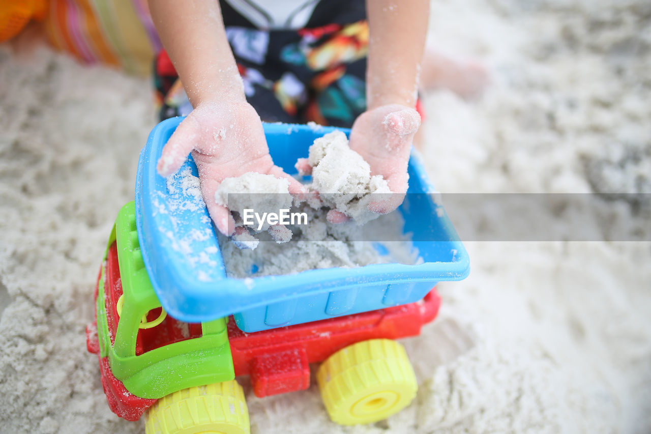 Midsection of boy holding sand above toy truck at beach