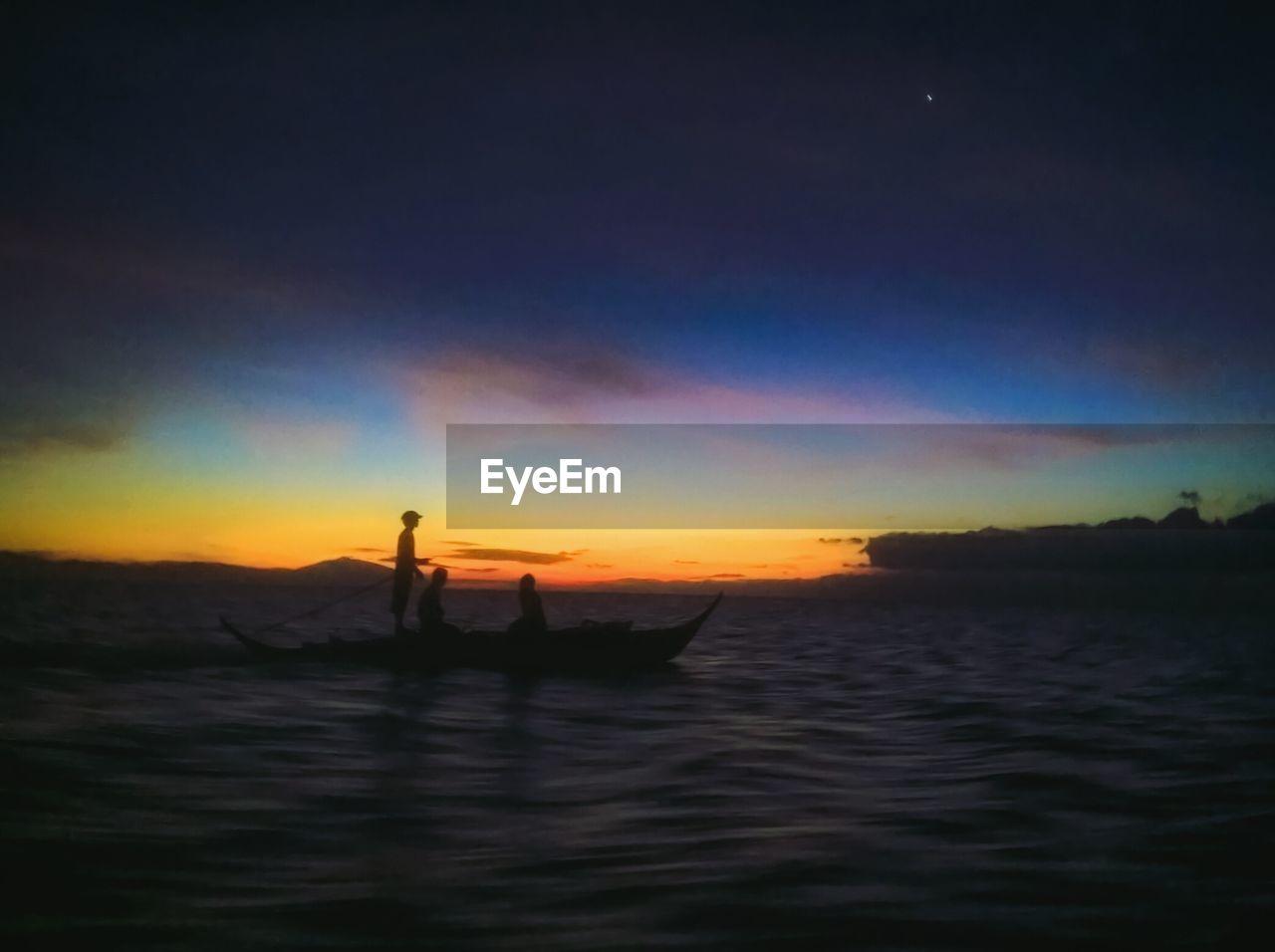 SILHOUETTE MEN SITTING ON SEA AGAINST SKY DURING SUNSET