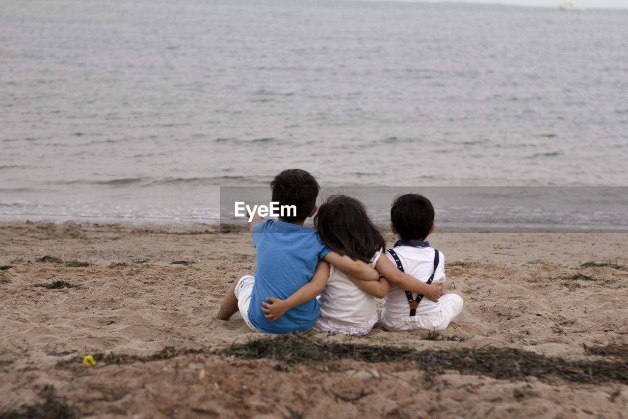 Three kids setting down on the sand while one of them is pointing