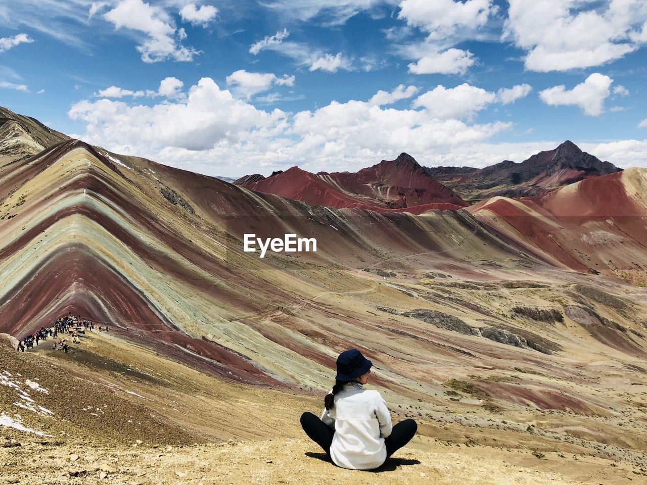 Rear view of woman sitting on mountain against sky