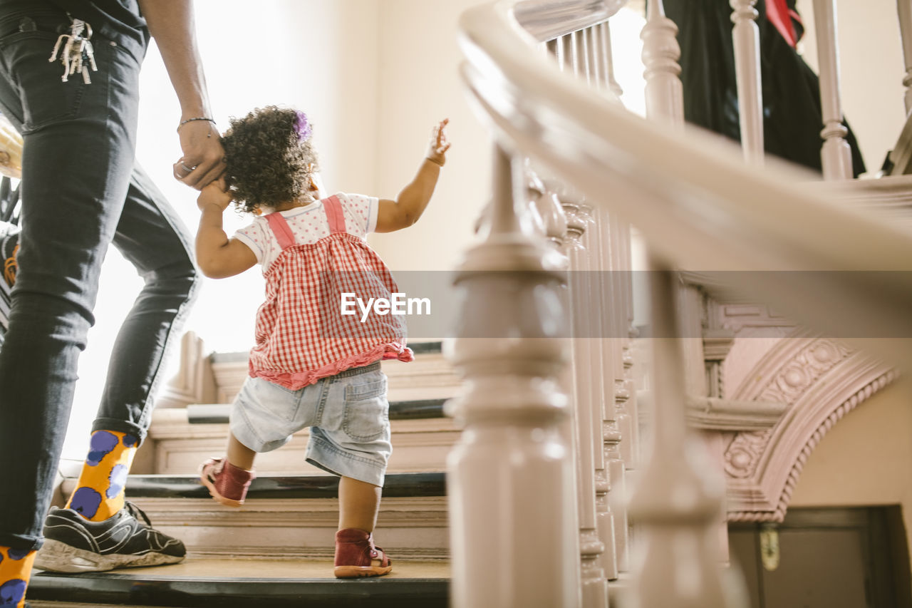 Baby girl holding hand of father while climbing steps in apartment