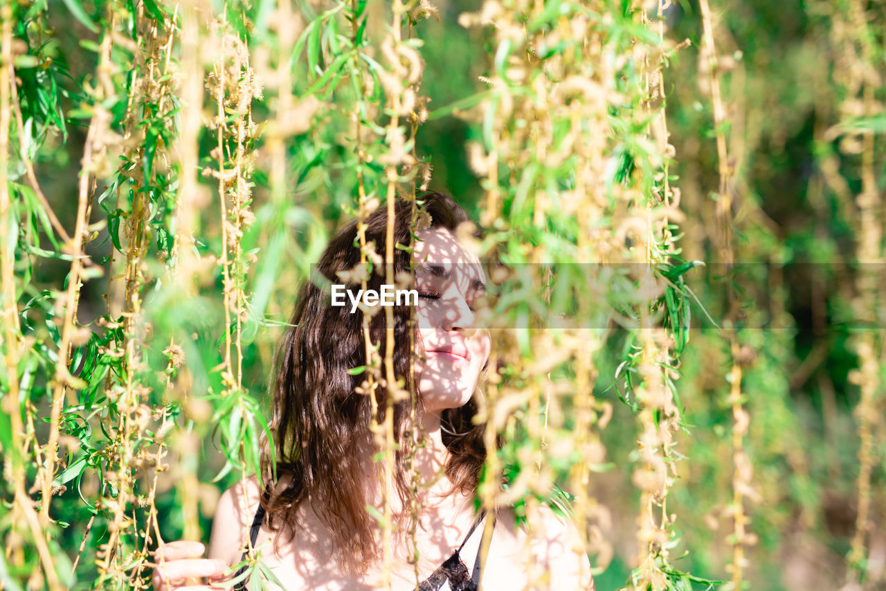 Woman with eyes closed standing by plants in park