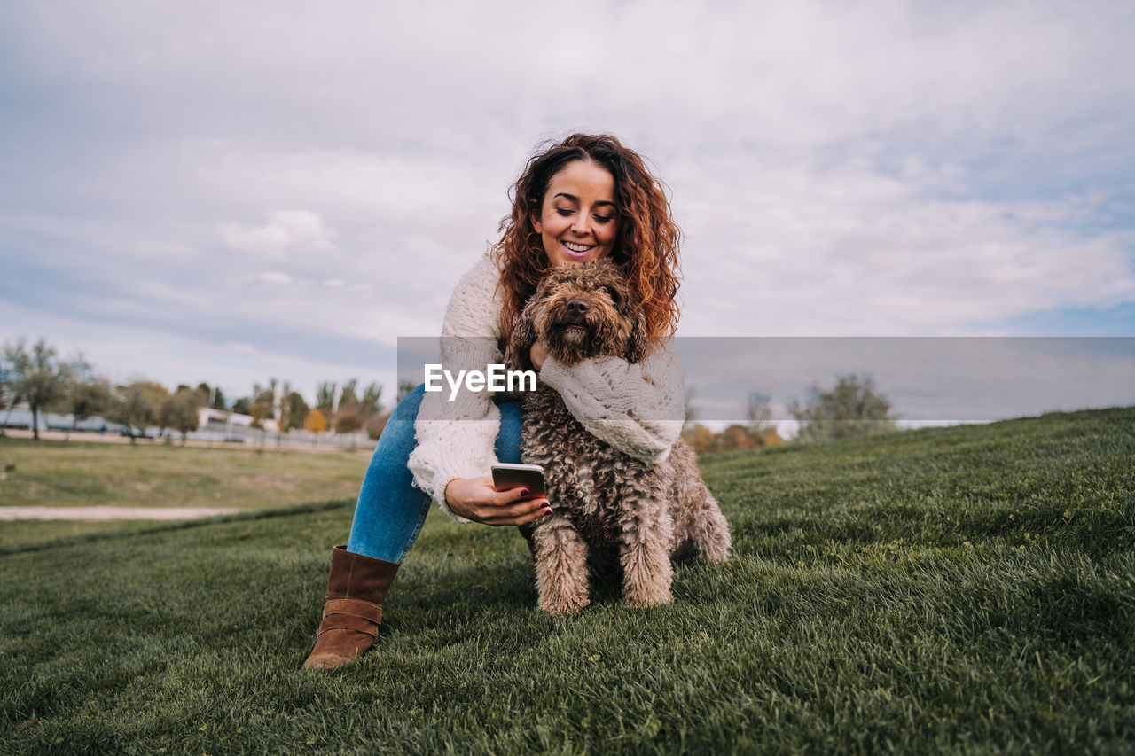 Smiling woman taking selfie with dog against sky