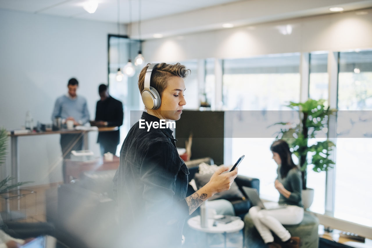 Female entrepreneur using smart phone while colleagues working in background