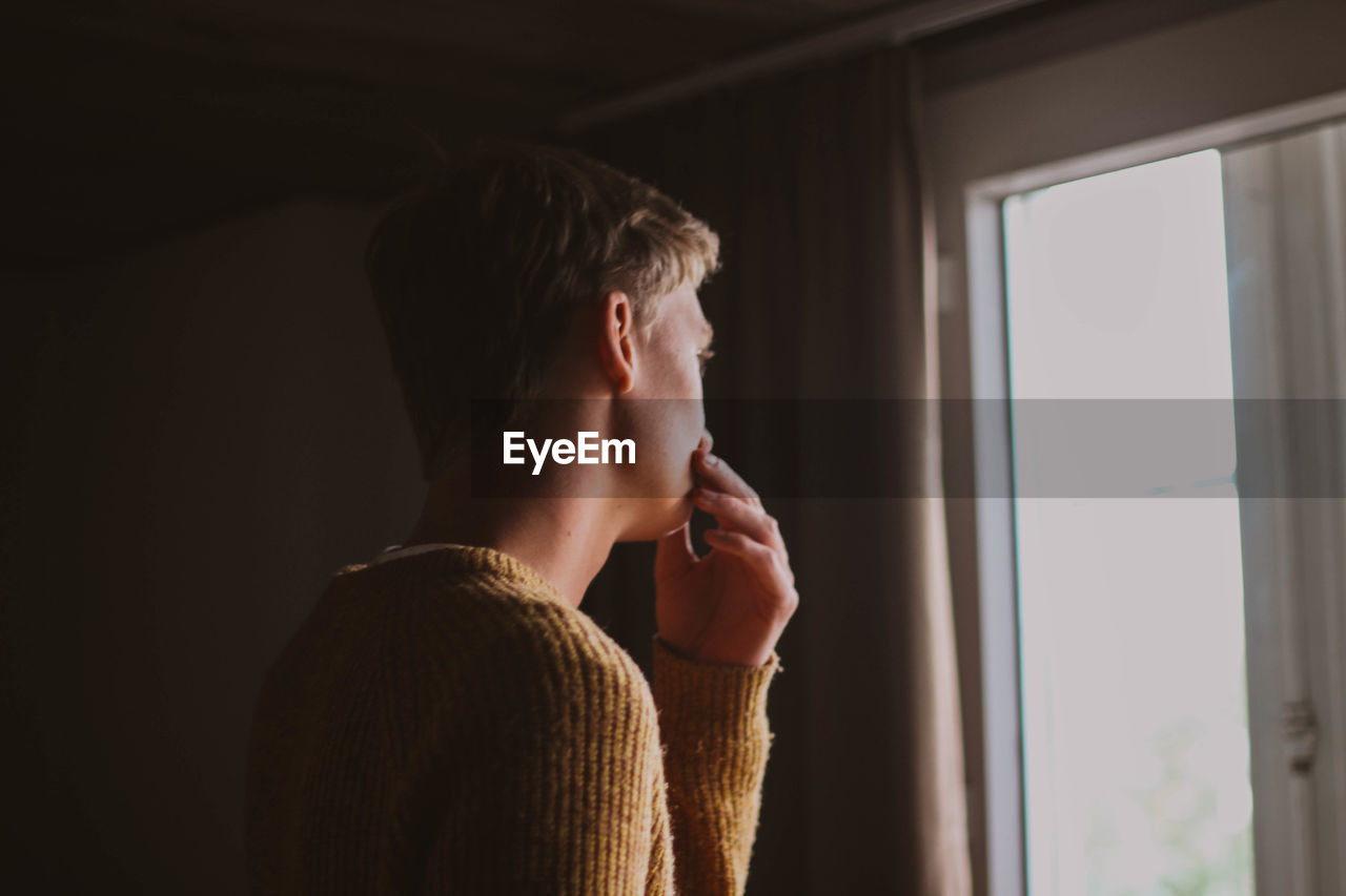 Portrait of man looking through window at home