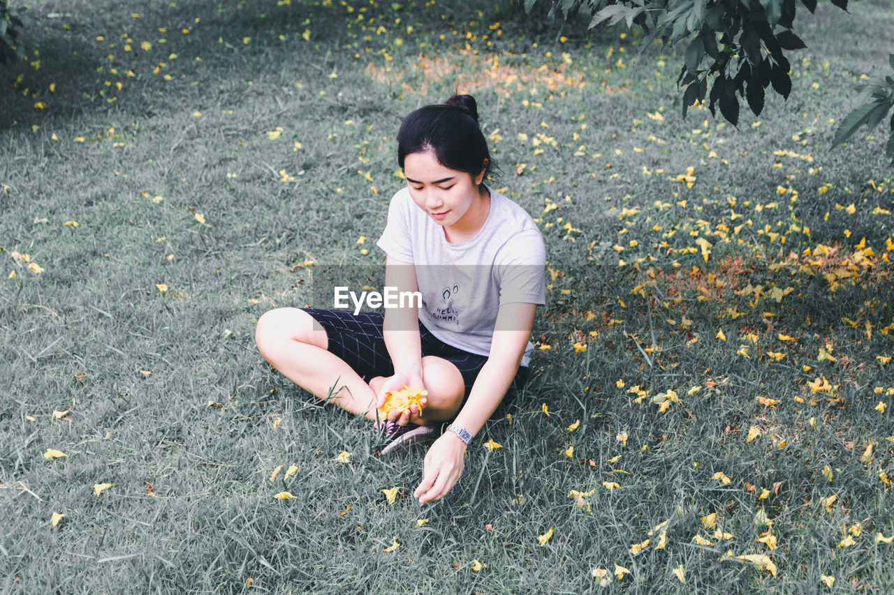 Woman picking flowers while sitting on field