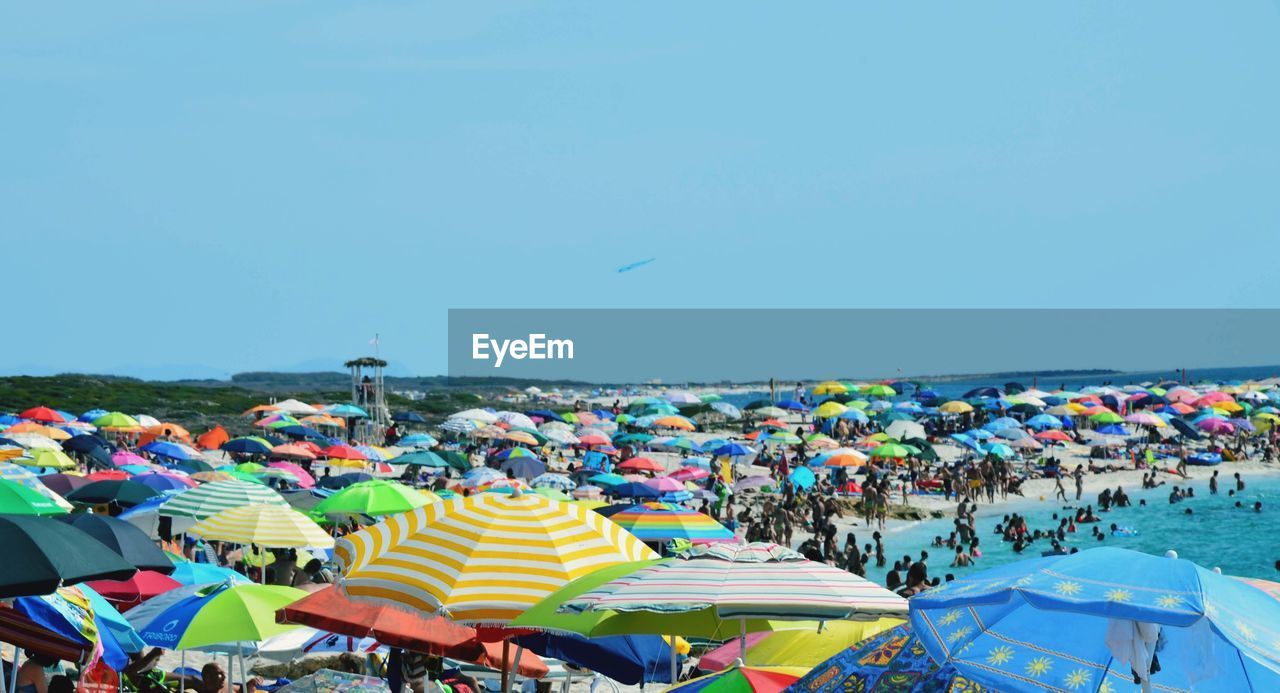 Crowd and colorful umbrellas against clear blue sky at beach