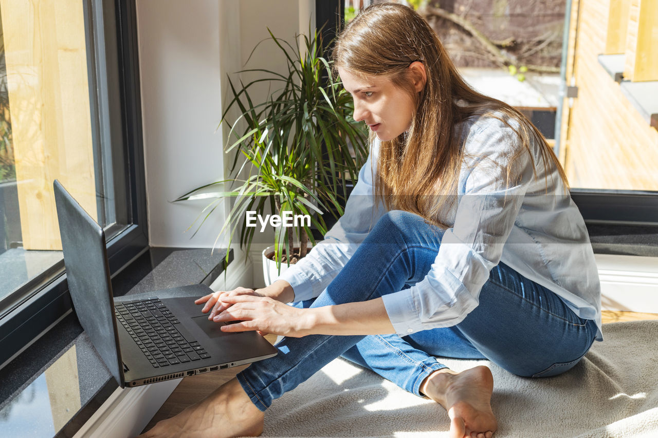 A girl sits on the floor in front of a laptop and makes purchases, chatting. work online. freelance