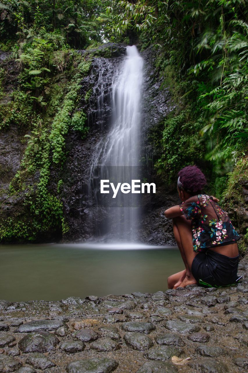 Woman sitting on rock looking at waterfall