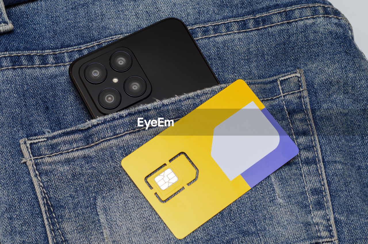 A modern smartphone in a jeans pocket and a new sim card of a telecom operator