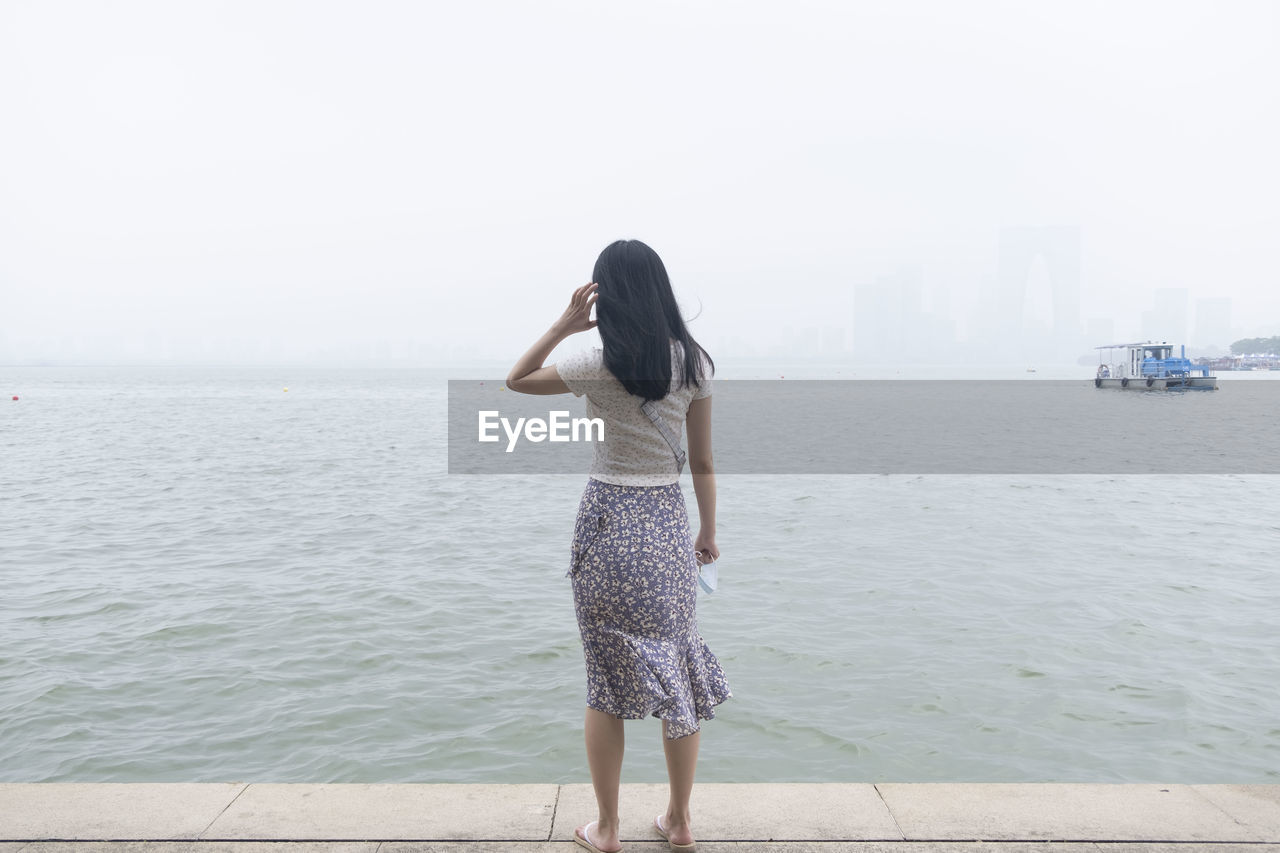 Rear view of young woman standing by sea against sky