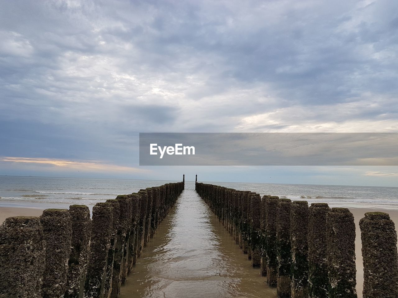 Wooden posts on sea against sky