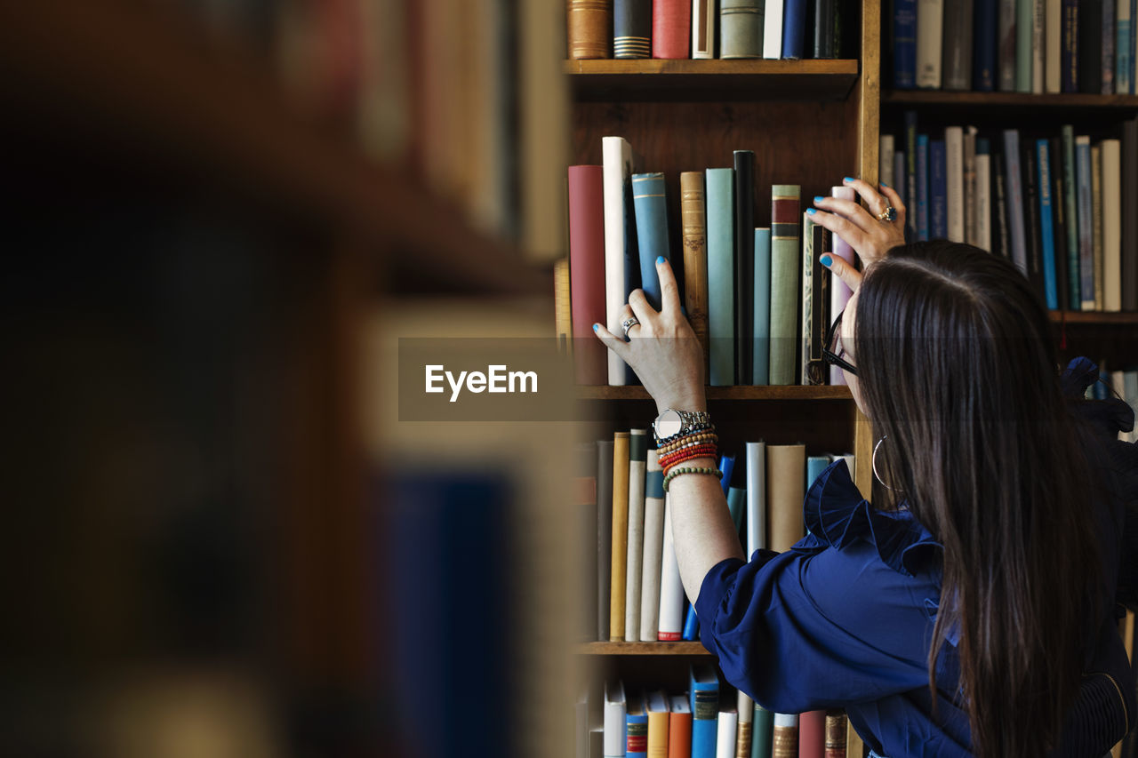 Rear view of woman searching book in library