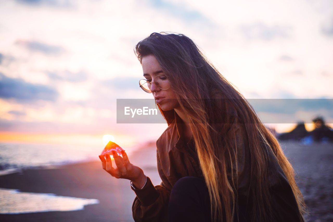 Young woman holding seashell at beach during sunset