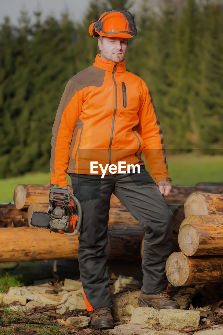 Portrait of lumberjack standing with chainsaw by logs