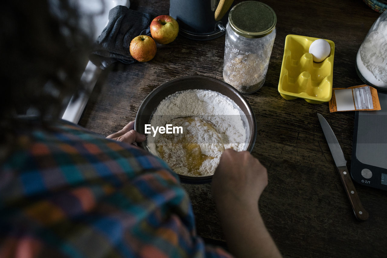 High angle view of woman mixing ingredient in flour on kitchen counter