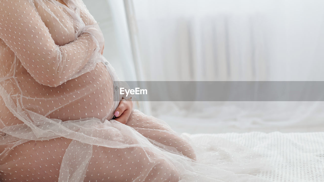 A happy pregnant woman holds her hands stomach sitting on a bed